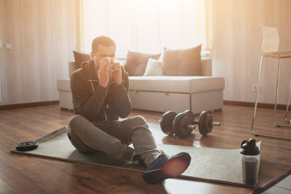 Young ordinary man go in for sport at home. Picture of spot beginner sitting on mat and sneezing. Sick and ill. Caught flu. Suffer from pain. Freshman in sport after or before workout got sick.